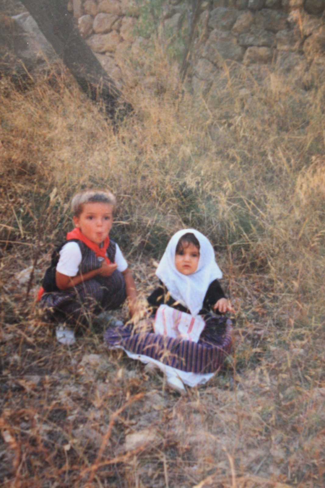 Shereen as a small child sitting in dry grass beside a cousin